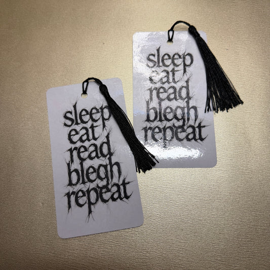 Weiße Lesezeichen mit schwarzen Quaste mit dem Schriftzug "sleep, eat, read, blech, repeat", Zwei Stück auf dem Bild.