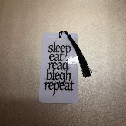 Weißes Lesezeichen mit schwarzen Quaste mit dem Schriftzug "sleep, eat, read, blech, repeat".