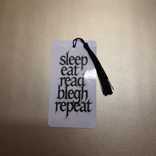 Weißes Lesezeichen mit schwarzen Quaste mit dem Schriftzug "sleep, eat, read, blech, repeat".
